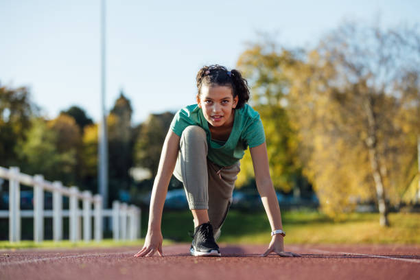 Front view of a young female child crouched down and ready to begin her sprint on an athletics track outside Wentworth Leisure Centre in Hexham, North East England. She is wearing sports clothing and she's focused on her sprint.
Video also available of this scenario.